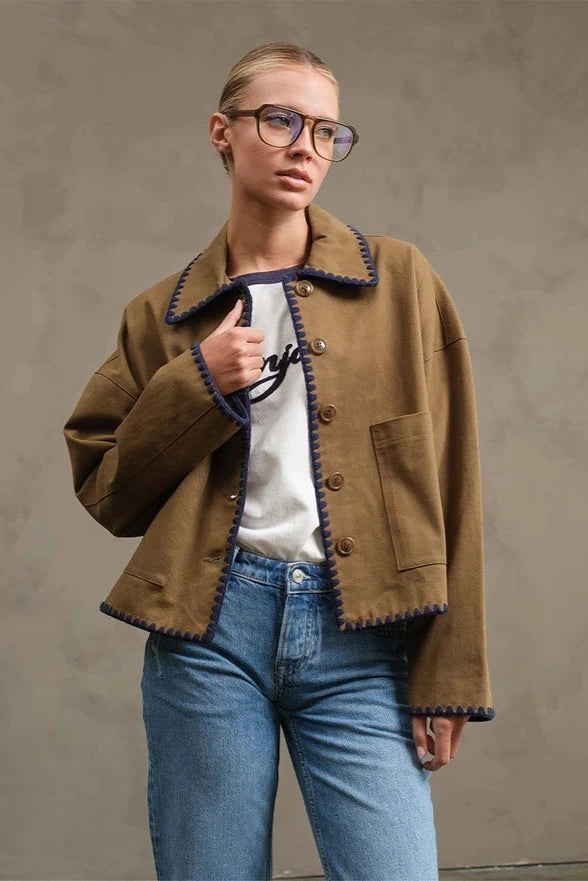 Person wearing a brown coat with blue jeans against a plain background