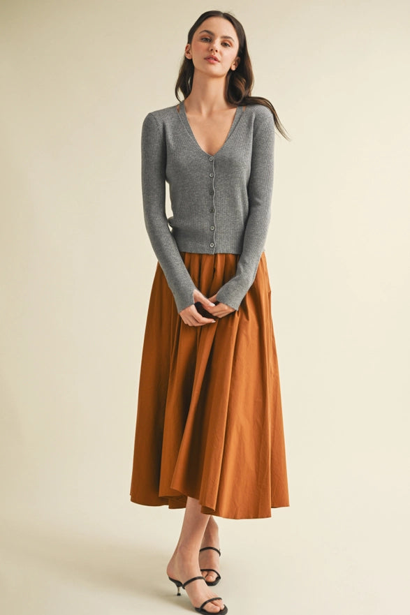 Woman wearing a gray cardigan and rust-colored skirt on a beige background