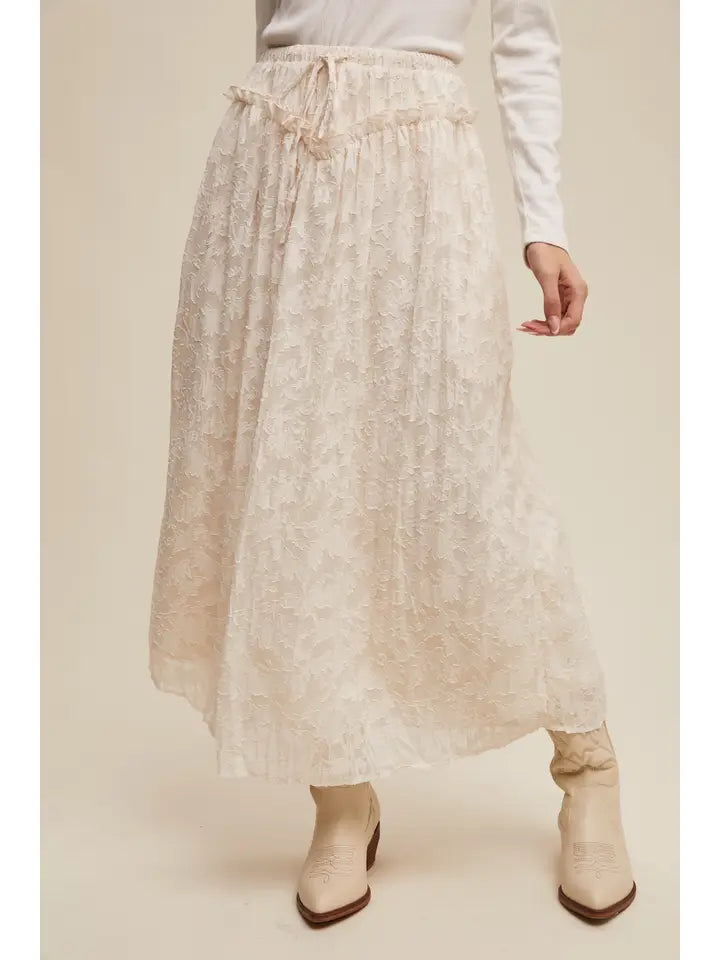 Person wearing a beige floral skirt and white top on a plain background