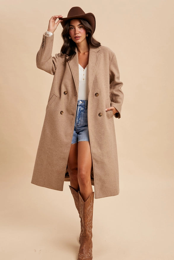 Woman wearing a long beige coat, denim shorts, and brown boots against a beige background