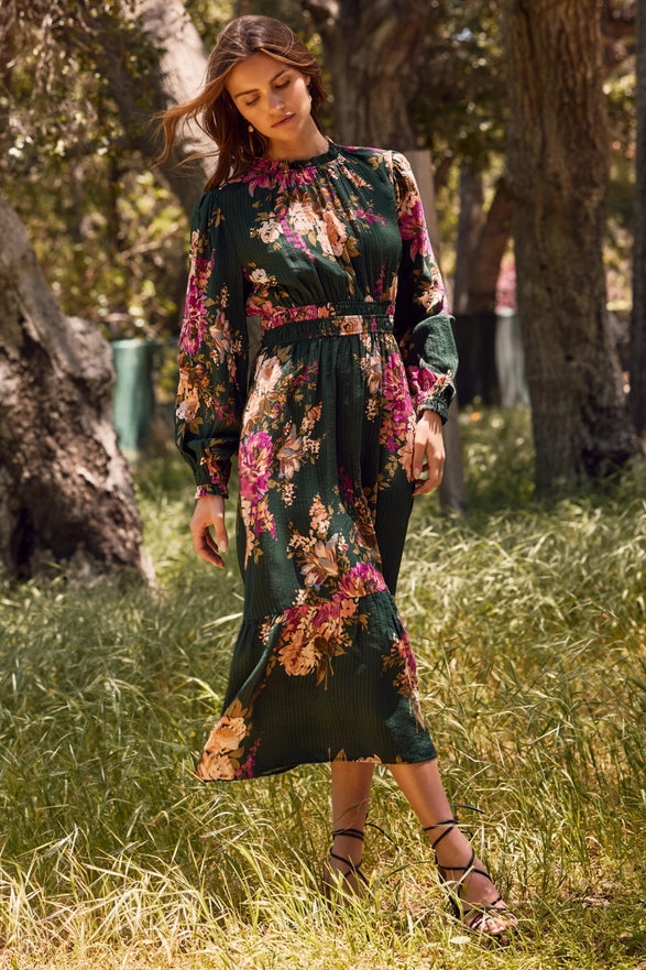 Woman in a floral dress standing in a grassy area with trees