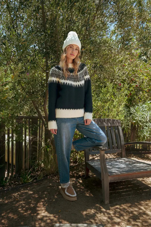 Person wearing a patterned sweater and jeans standing outdoors with trees in the background