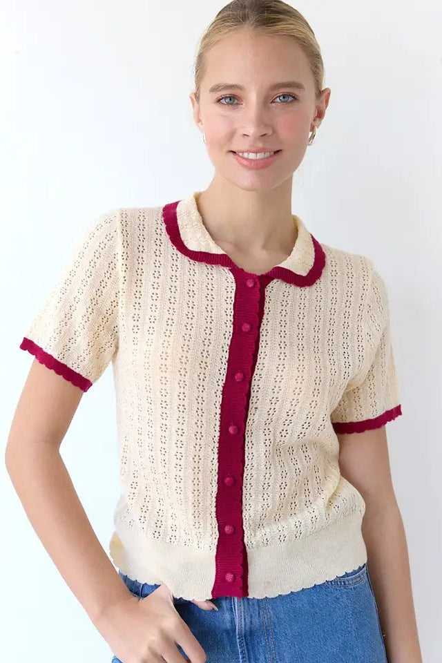 Woman wearing a cream lace cardigan with red trim and buttons on a white background