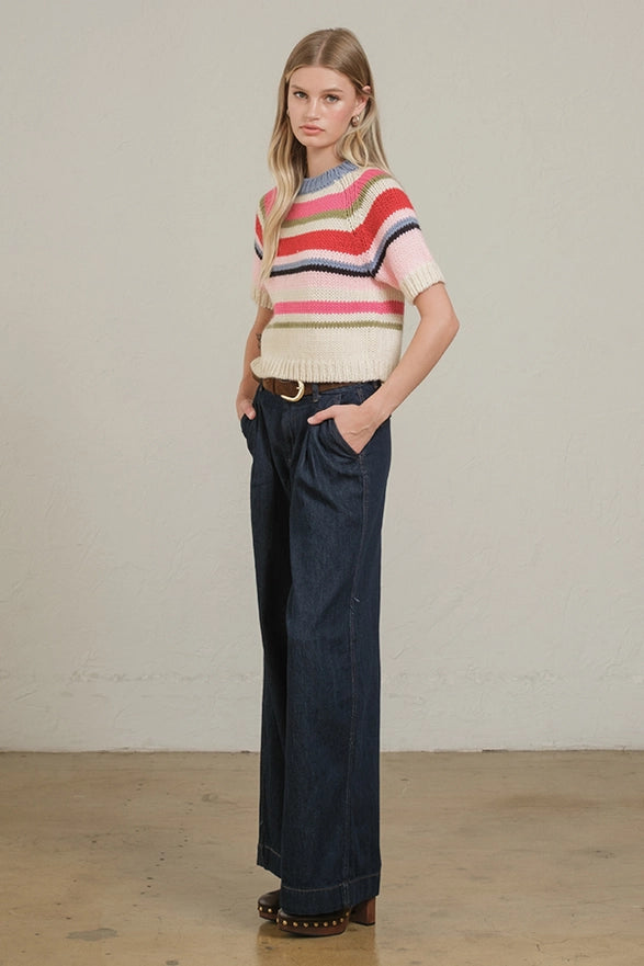 Woman wearing a colorful striped sweater and dark jeans against a plain background