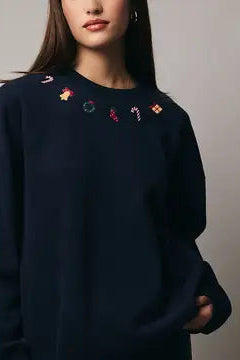 Person wearing a navy blue sweatshirt with embroidered designs on a plain background
