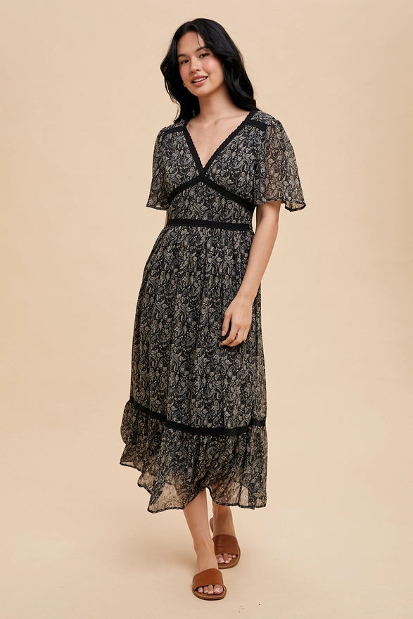 Woman wearing a black midi dress with flutter sleeves on a plain background