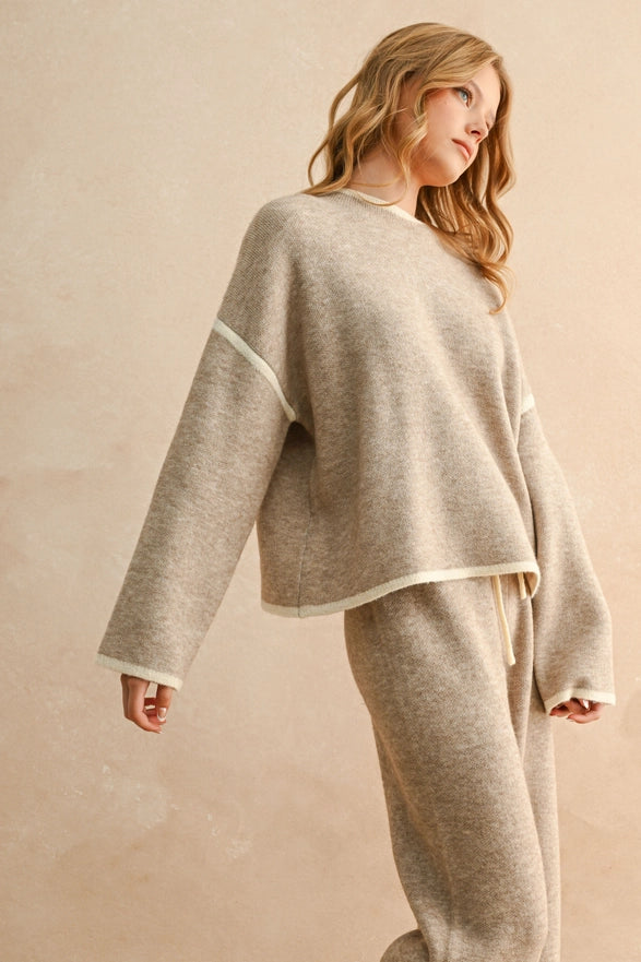 Woman wearing a beige sweater and pants set against a beige background