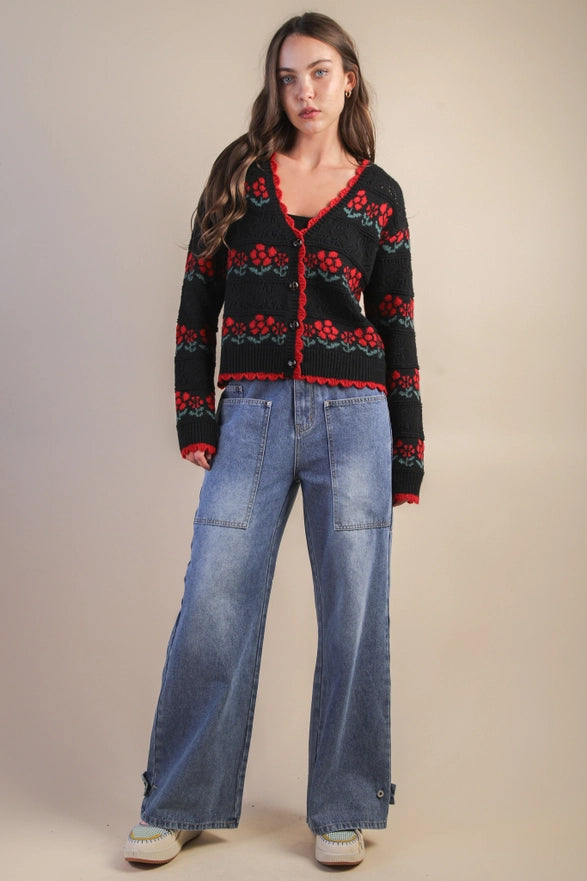 Woman wearing a black cardigan with red patterns and blue jeans on a beige background