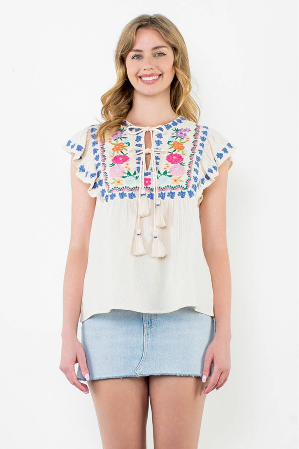 Woman wearing a white blouse with floral embroidery and a denim skirt on a white background