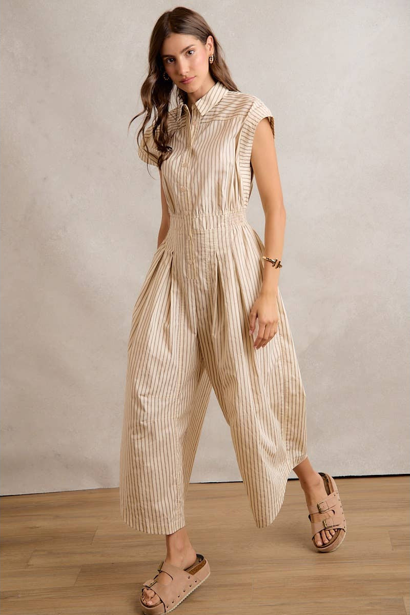 Woman wearing a beige striped jumpsuit standing against a plain background