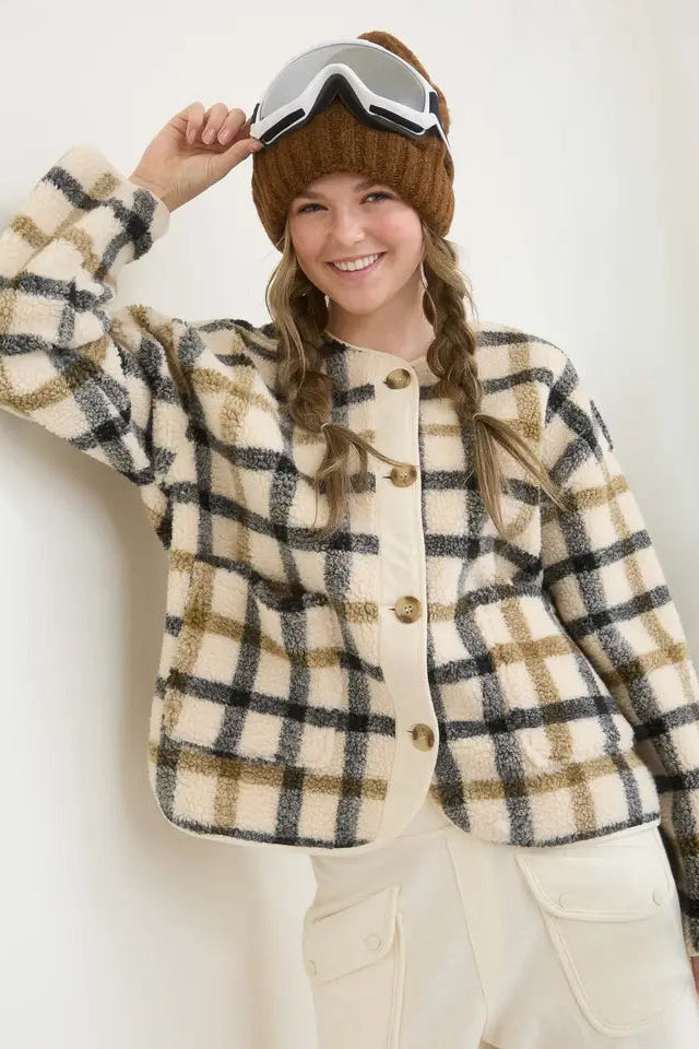 Person wearing a plaid jacket and goggles, standing against a white wall with a Christmas tree in the background.