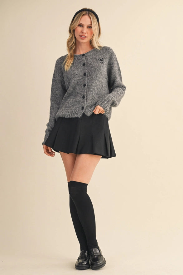 Woman wearing a gray cardigan, black skirt, and knee-high socks on a beige background