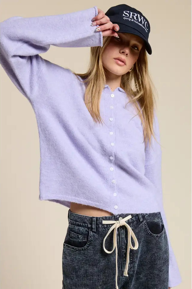 Person wearing a light purple shirt, black cap with 'SRWC' logo, and dark jeans on a beige background