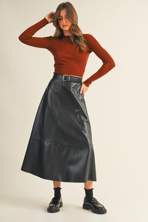 Woman wearing a rust-colored long-sleeve top and black leather skirt on a beige background