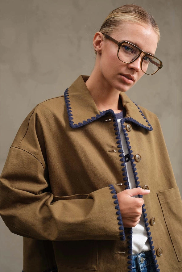 Person wearing a brown coat with blue trim against a neutral background