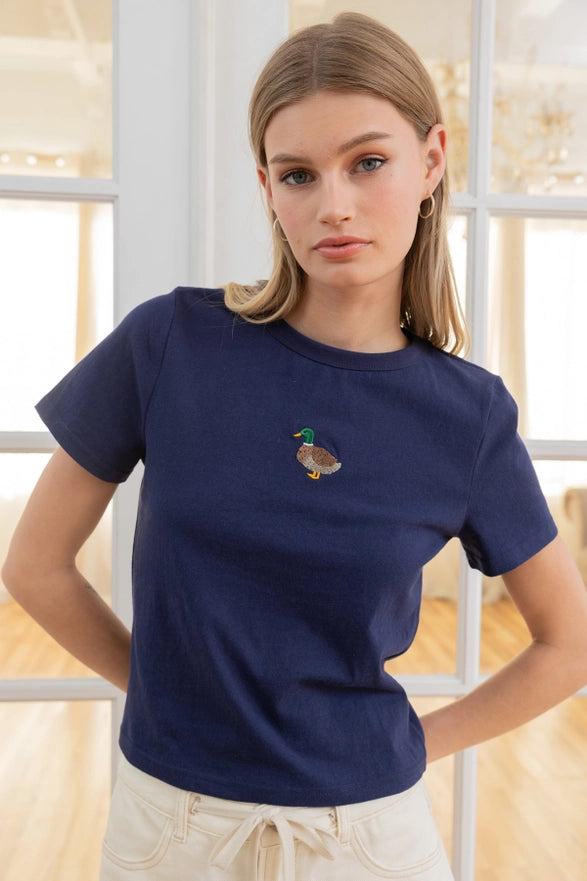 Woman wearing a navy blue t-shirt with a duck design in a bright room.