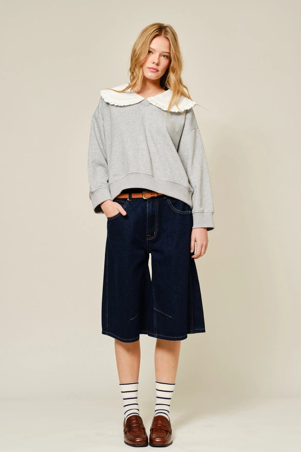 Woman wearing a gray oversized sweater with a white collar, navy shorts, and brown shoes on a beige background