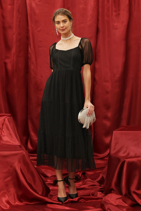 Woman in a black dress standing against a red curtain backdrop