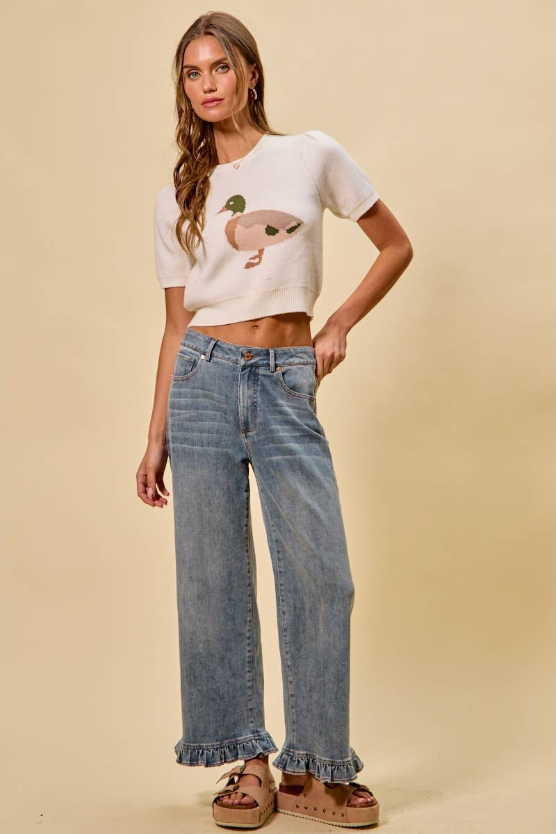 Woman wearing a white cropped sweater with a graphic design and blue jeans on a beige background