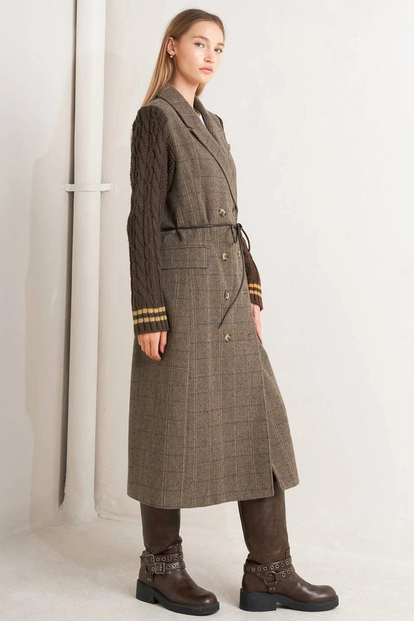 Woman wearing a long brown coat with a patterned belt against a white background