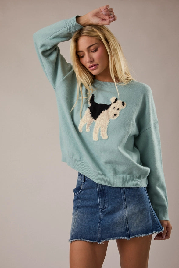 Woman wearing a light blue sweater with a dog design against a beige background