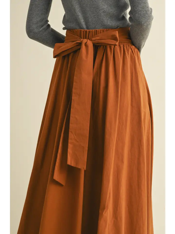 Person wearing a rust-colored skirt with a belt on a beige background