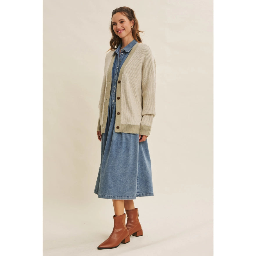 Woman wearing a beige cardigan, denim shirt, and skirt with brown boots on a plain background