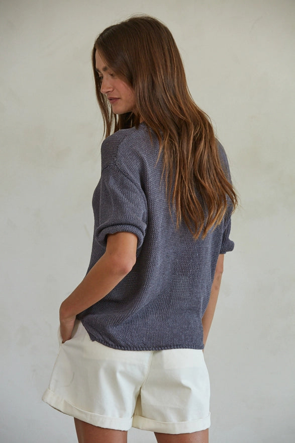 Woman wearing a blue sweater and white shorts against a plain background