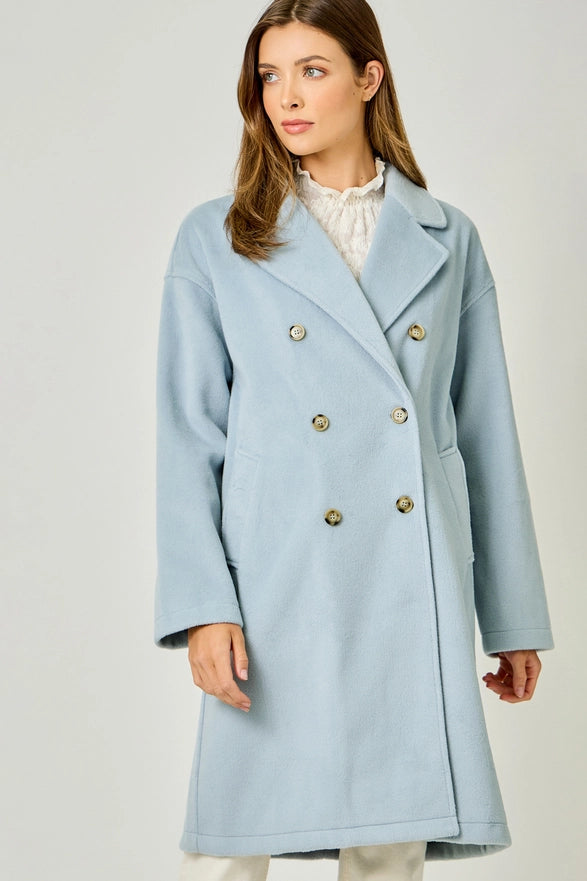 Woman wearing a light blue coat with gold buttons on a plain background