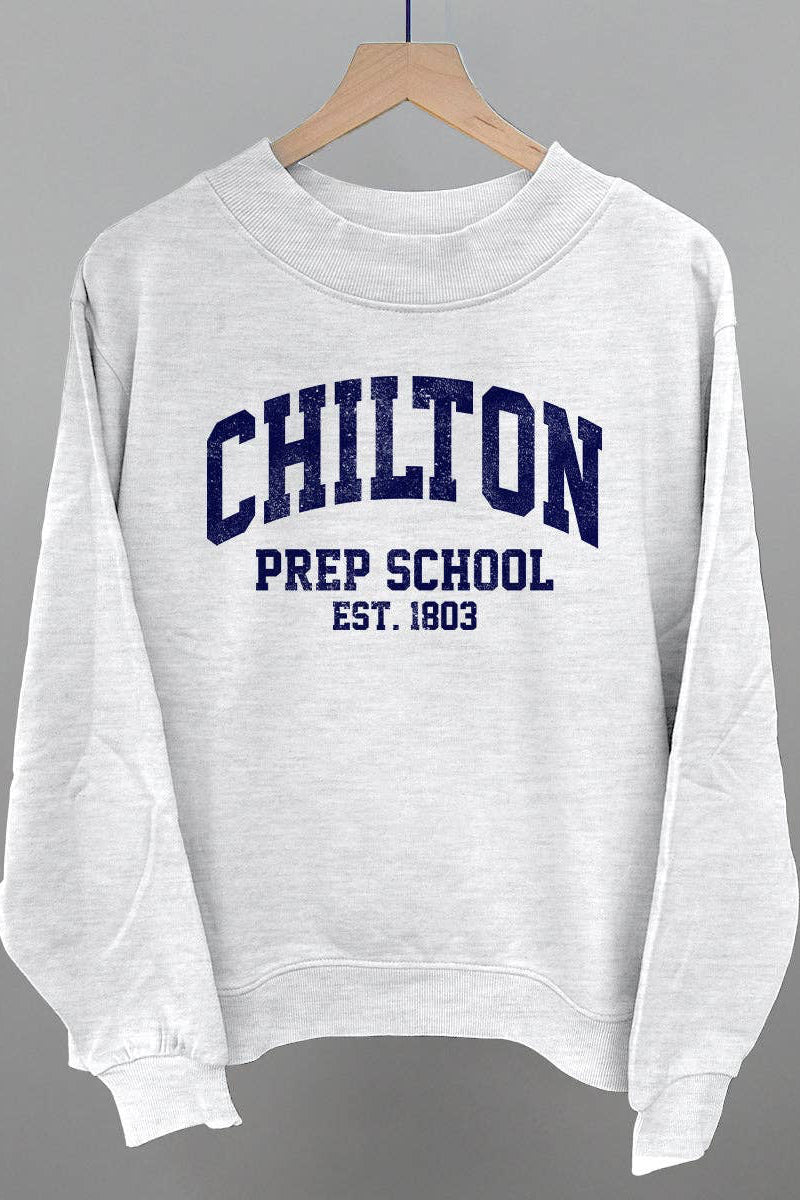 A white crewneck sweatshirt hanging on a wooden hanger against a neutral gray background. The sweatshirt features navy blue collegiate-style text reading 'CHILTON PREP SCHOOL EST.