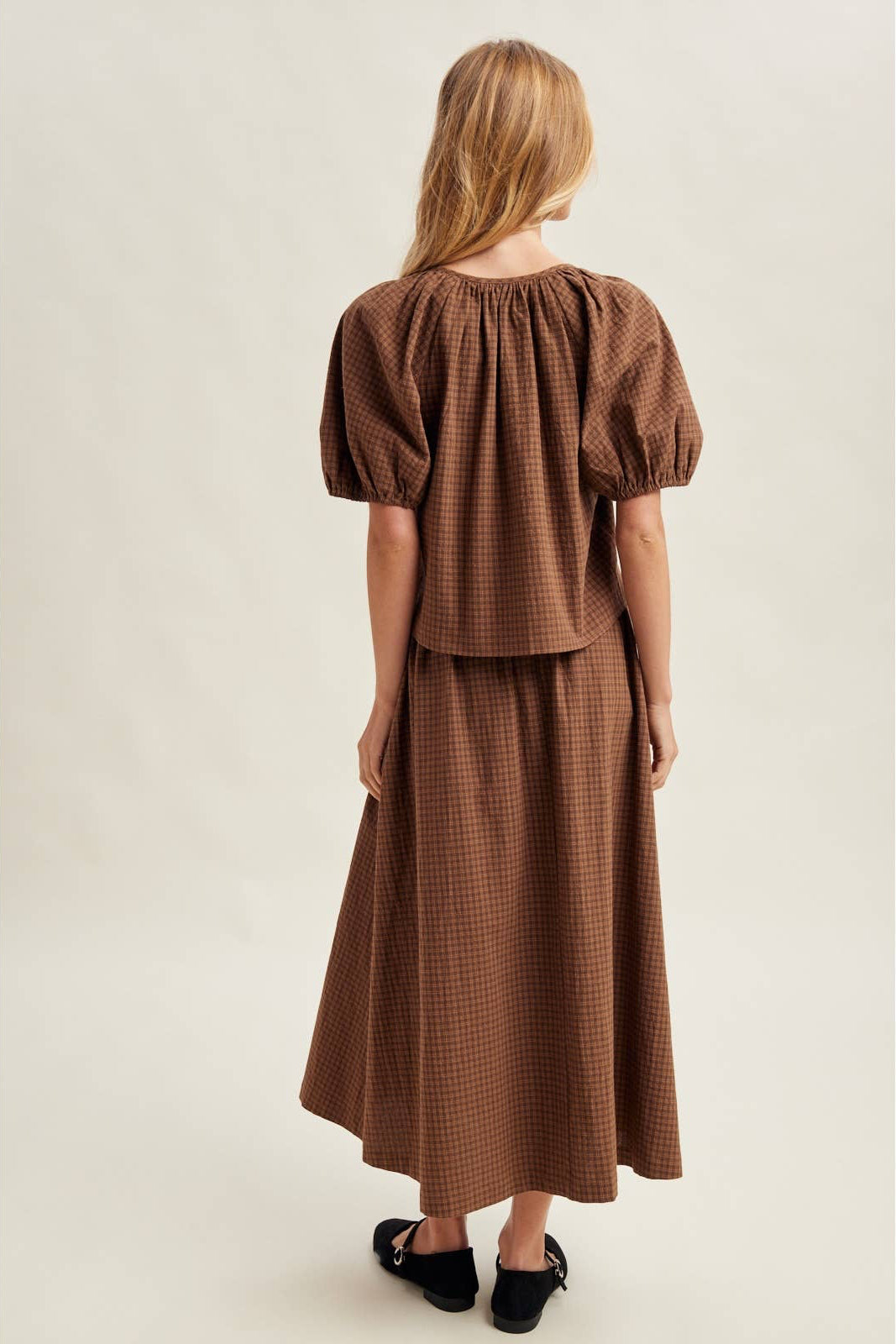 Woman wearing a brown checkered dress against a plain background