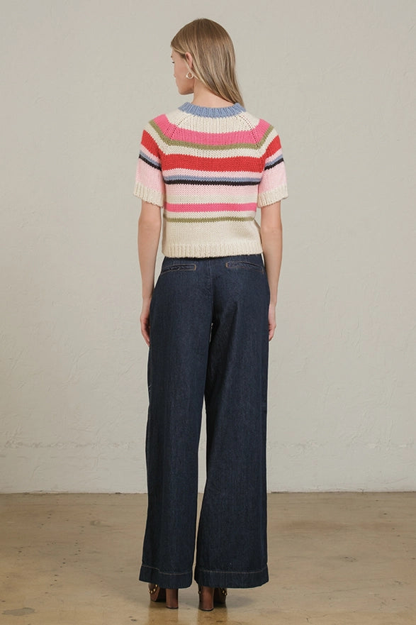 Woman wearing a colorful striped sweater and dark jeans against a plain background