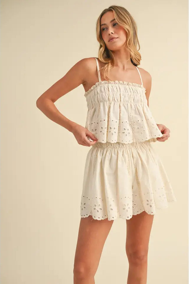 A woman wearing a beige embroidered cami top and matching shorts with lace trim.