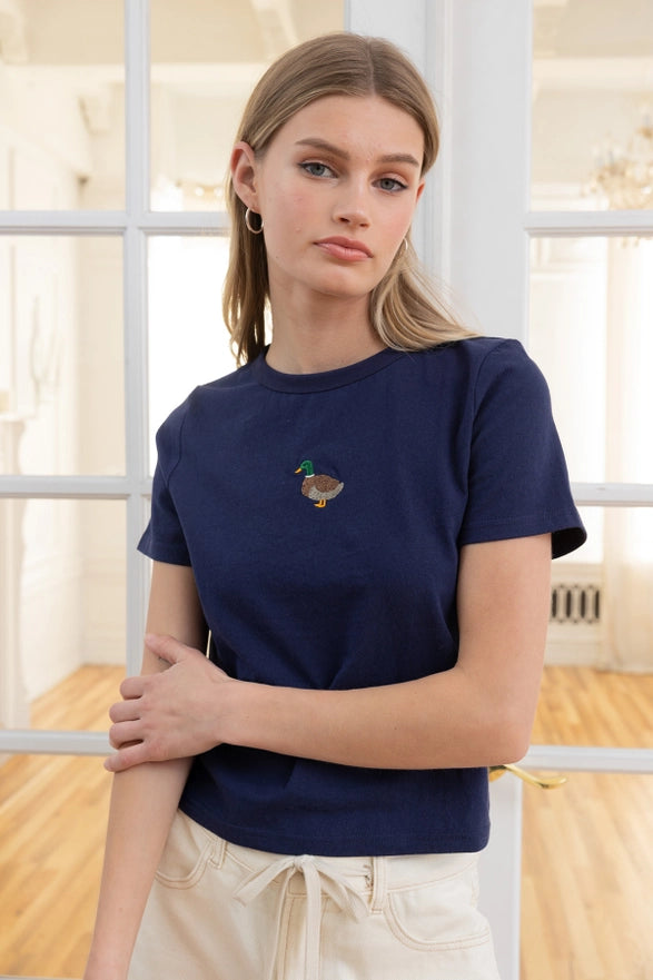 Woman wearing a navy blue t-shirt with a small graphic design, standing indoors.