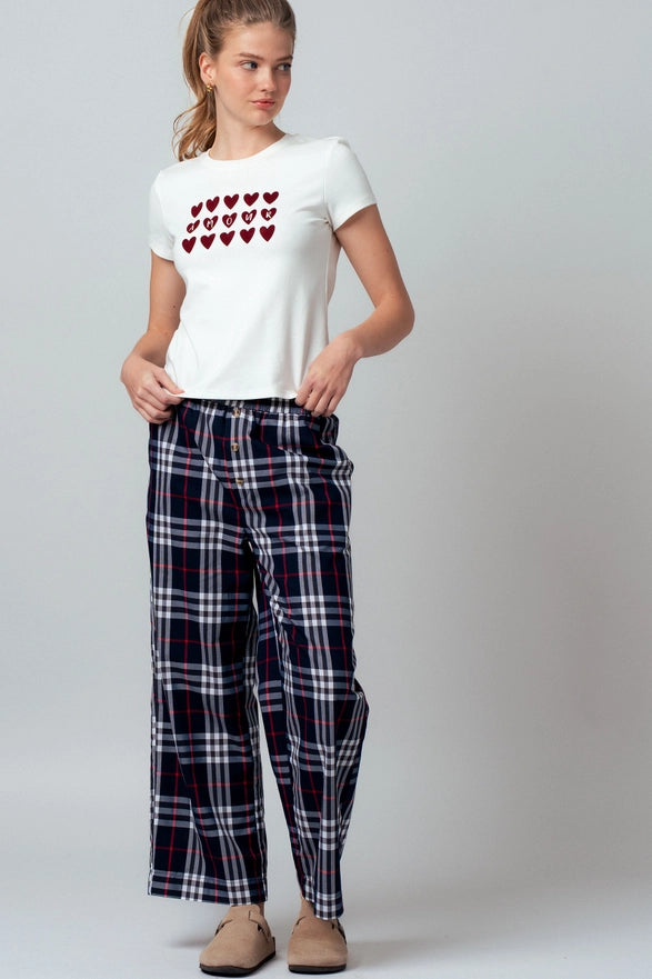 Woman wearing a white t-shirt with heart design and plaid pants on a gray background