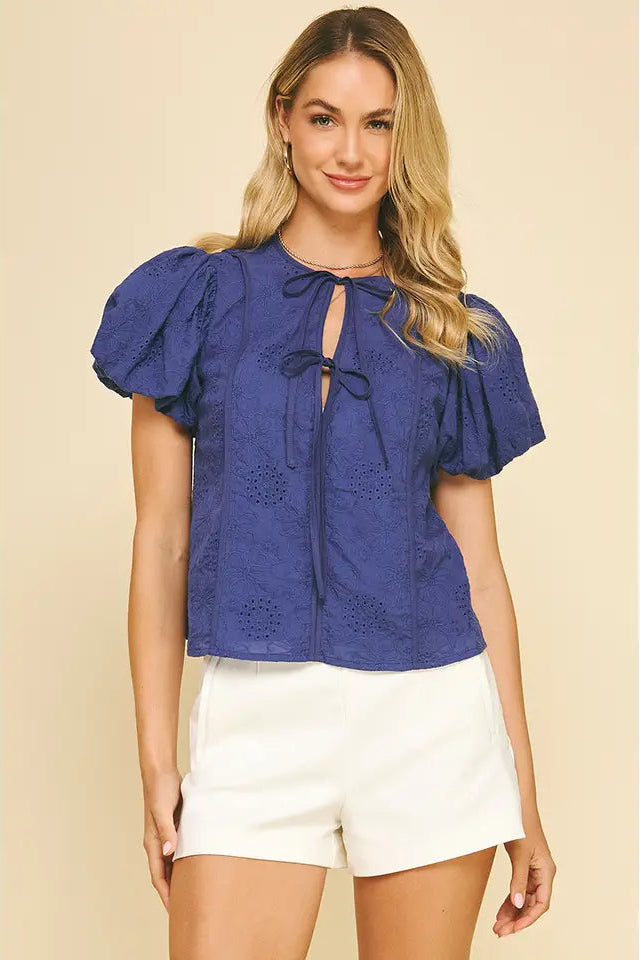 Woman wearing a blue blouse with puff sleeves and white shorts on a beige background