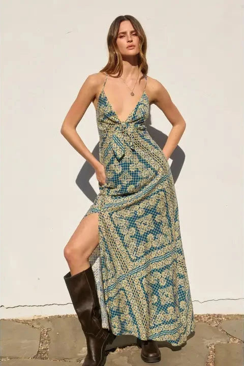 Woman in a patterned dress and knee-high boots against a white wall.