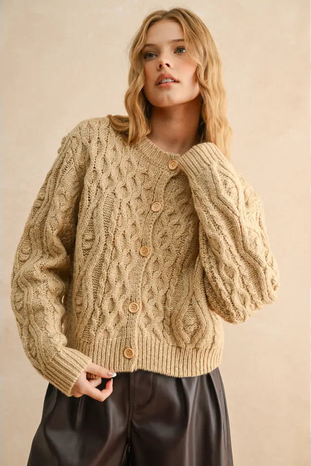 Woman wearing a beige cable knit sweater with buttons against a beige background