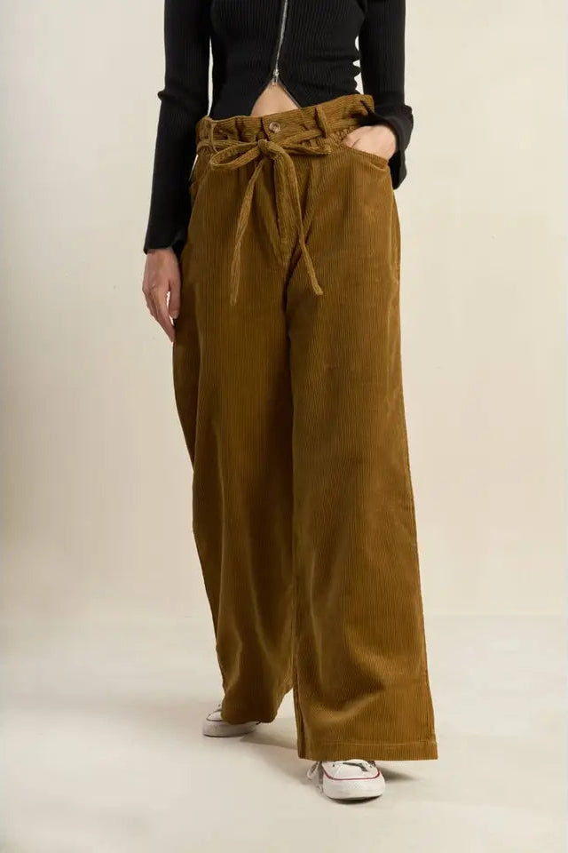 Person wearing brown wide-leg pants with a tie-waist design on a plain background
