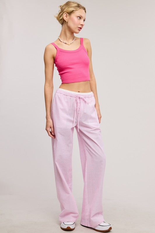 Woman wearing a pink tank top and pink sweatpants on a light gray background