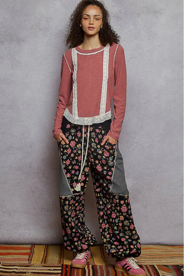 Woman wearing a pink top and floral pants against a gray wall.