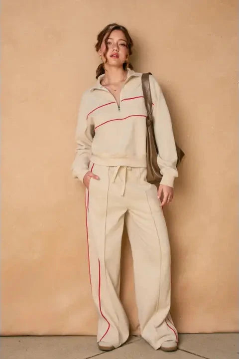 Woman wearing a beige tracksuit with red accents against a beige wall.
