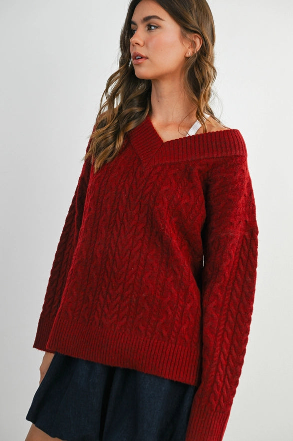 Girl Standing against a plain background wearing a V neck Wine Blue cable knit sweater with long sleeve