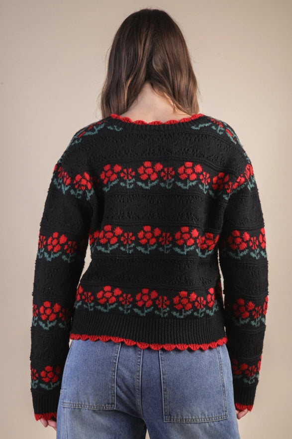 Person wearing a black sweater with red and green floral patterns on a beige background