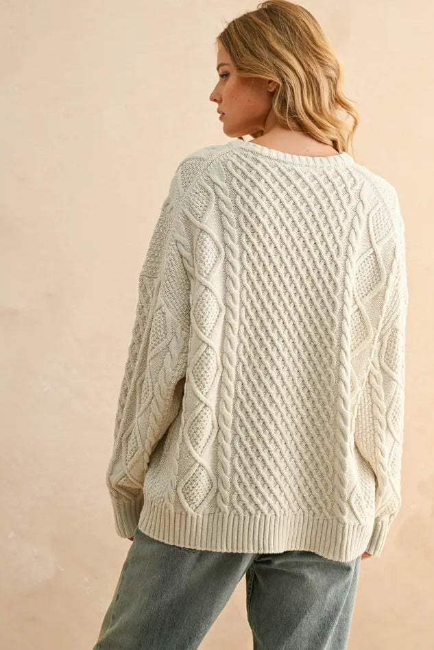 Woman wearing a cream cable knit sweater against a beige background