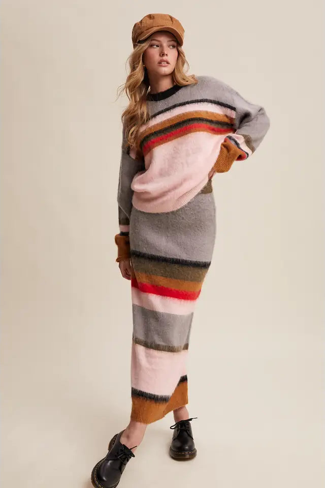 Woman wearing a long, colorful striped sweater dress with a beige cap on a plain background