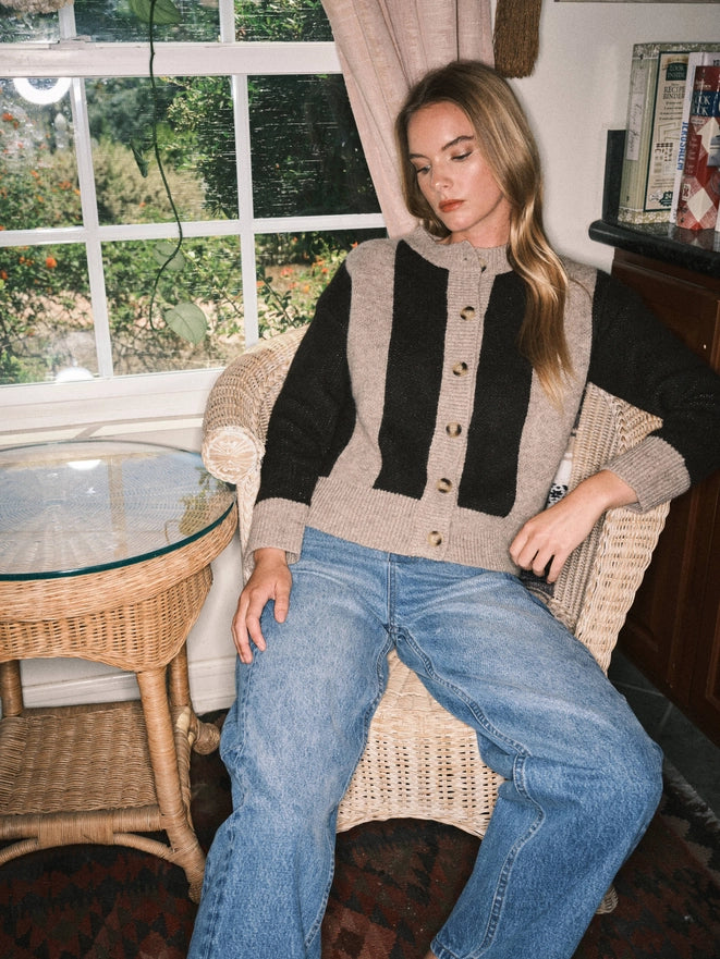 Woman sitting on a chair wearing a black and beige cardigan with a striped pattern.