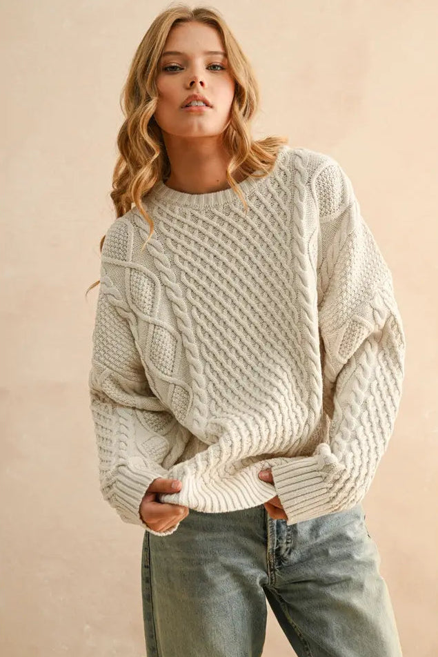 Woman wearing a beige cable knit sweater against a beige background