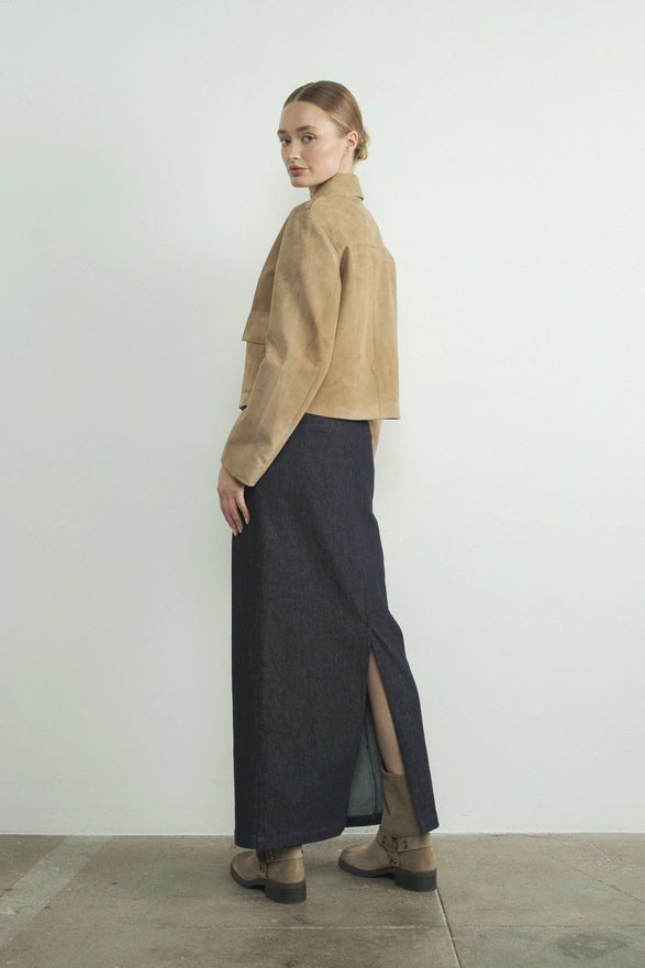 Woman wearing a beige jacket and dark gray skirt with a slit on a white background