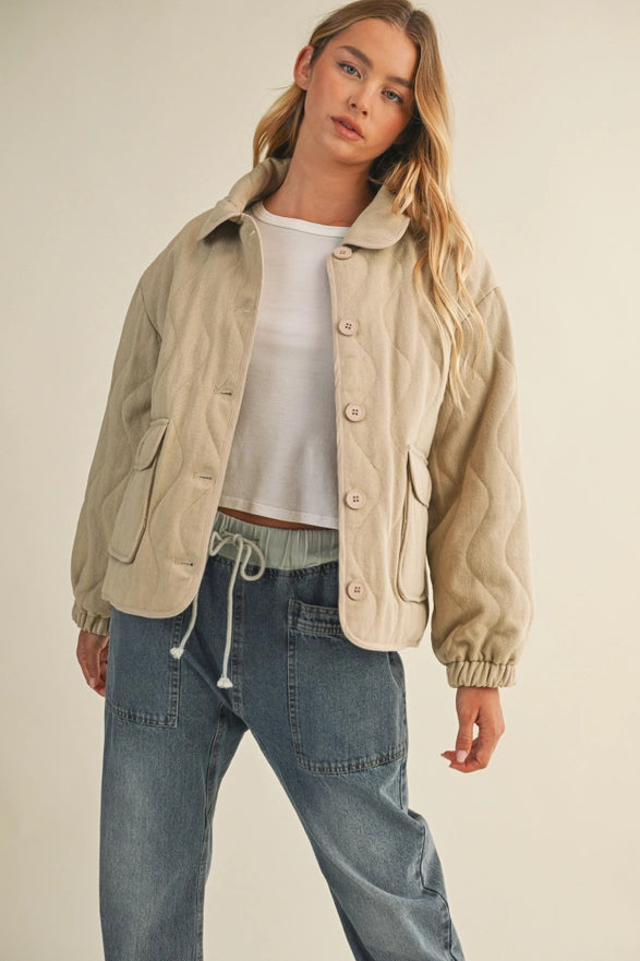Woman wearing a beige jacket and blue jeans on a plain background